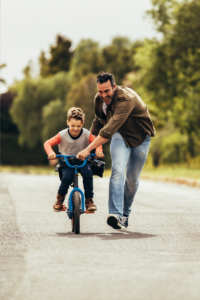 Dad teaching child to ride a bike - positive consequences, teaching and guiding, not punishing